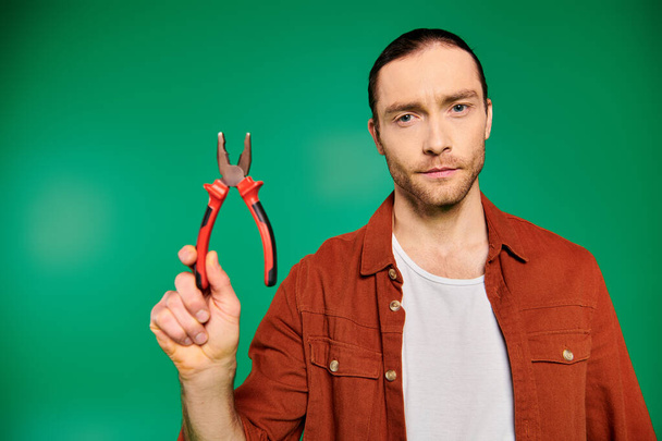 Handsome worker holding scissors in hand on green backdrop. - Photo, Image