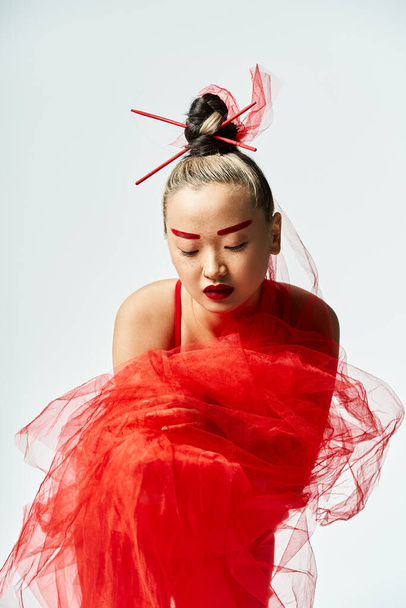 Привлекательная азиатка занимает изящную позу в ярком красном платье и вуали. - Фото, изображение