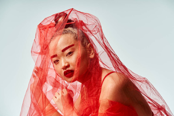 Kırmızı elbiseli çekici bir Asyalı kadın kafasında peçeyle dinamik bir poz veriyor.. - Fotoğraf, Görsel