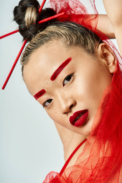 Una atractiva asiática vestida con ropa vibrante, con maquillaje rojo y un velo rojo en la cabeza. - Foto, Imagen