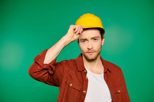 Ein gutaussehender männlicher Arbeiter in Uniform und Werkzeug mit gelbem Hut vor grünem Hintergrund. - Foto, Bild