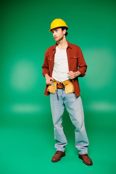 Een man met een harde hoed met een gereedschapsriem, klaar om te werken op een groene achtergrond. - Foto, afbeelding