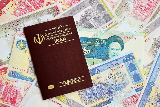 Red Islamic Republic of Iran passport and iranian reals money bills background close up. Tourism and travel concept - Photo, Image