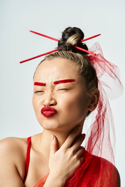 Mujer asiática adornada con maquillaje rojo y un velo, exudando elegancia y misterio. - Foto, Imagen