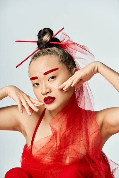 Une femme asiatique captivante dans une robe rouge vibrante, les mains sur la tête. - Photo, image