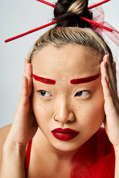 Atrakcyjna Azjatka z czerwonym makijażem trzymająca głowę dramatycznie. - Zdjęcie, obraz