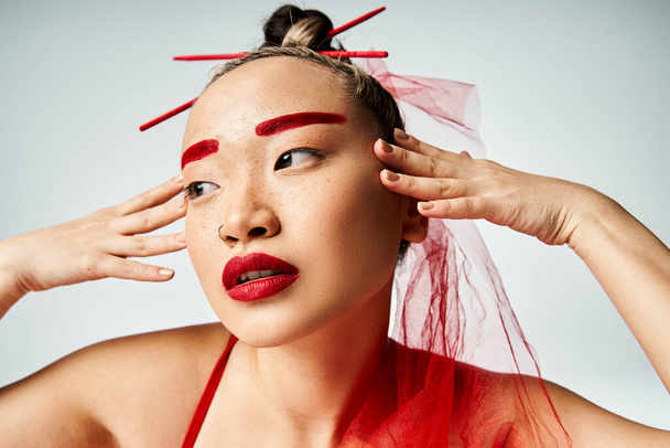 Femme asiatique avec un maquillage rouge frappant portant un voile, exsudant élégance et mystère. - Photo, image