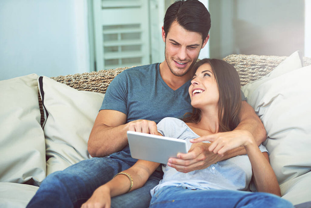 Happy couple, hug and sofa with tablet for movie, social media or entertainment at home. Man and woman lying in relax with smile on technology for online streaming, series or show in living room. - Photo, Image