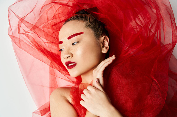 Kafasında peçesi olan canlı kırmızı elbiseli çekici bir Asyalı kadın zarif bir poz veriyor.. - Fotoğraf, Görsel