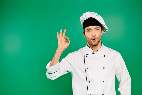 Knappe man chef-kok in wit uniform maken OK teken op groene achtergrond. - Foto, afbeelding