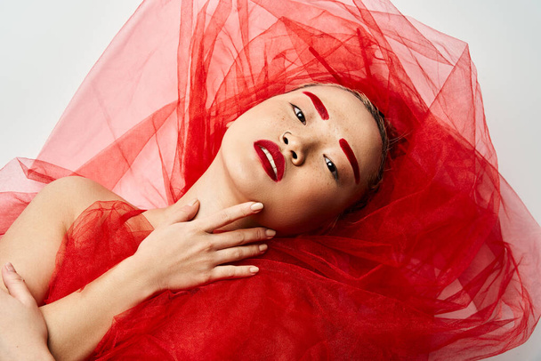 Een opvallende Aziatische vrouw in een levendige rode jurk en bijpassende lippenstift poseert zelfverzekerd. - Foto, afbeelding