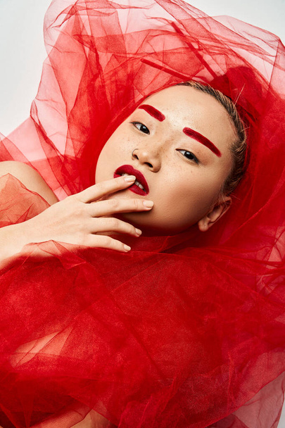 Opvallende aziatische vrouw in levendige rode make-up en jurk stakingen een boeiende pose. - Foto, afbeelding