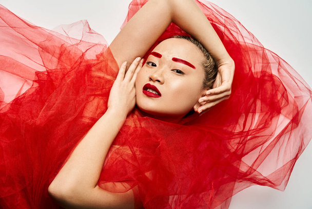 Elegante Aziatische vrouw poseert in rode jurk met handen op het hoofd. - Foto, afbeelding