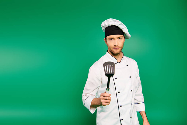 Un chef con uniforme blanco empuña una espátula sobre un fondo verde. - Foto, imagen