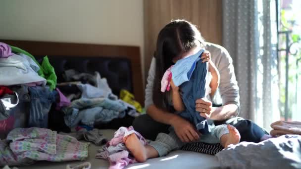 Мама и маленькая девочка играют в сортировку стиральной одежды, разбрасывая ее по кровати. Высококачественные 4k кадры - Кадры, видео