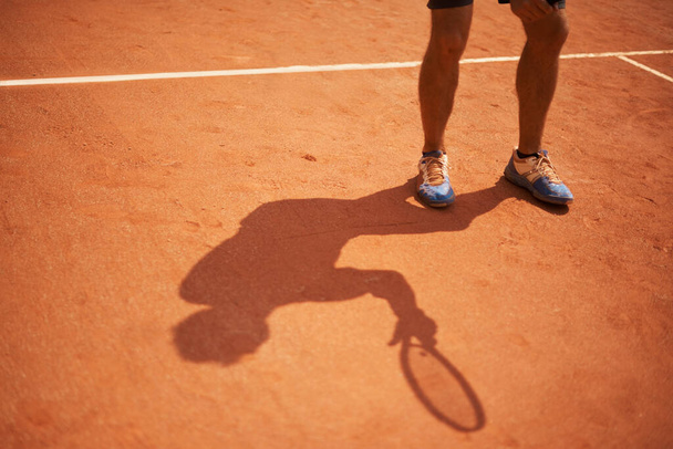Τένις, το δικαστήριο και τα παπούτσια του αθλητή εξωτερική κατά την έναρξη της άσκησης της προπόνηση στο διαγωνισμό. Πρόσωπο, σκιά και sneakers στα πόδια του παίκτη εκπαίδευση σε πηλό γήπεδο στο παιχνίδι του αθλητισμού με καλή φυσική κατάσταση ή δράση. - Φωτογραφία, εικόνα