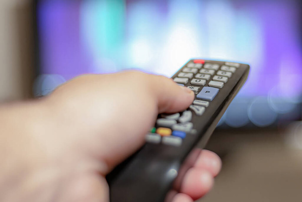 Una persona con un control remoto de TV controla el control remoto para cambiar los canales para ver programas de televisión
. - Foto, imagen