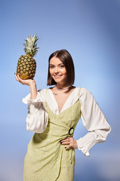 ブルネットの髪を持つ若い女性は喜んでスタジオの設定で彼女の顔にパイナップルを保持します. - 写真・画像