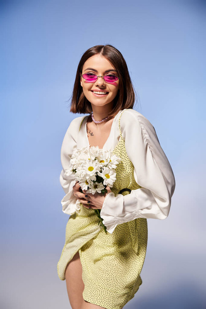 Brünette Frau in elegantem Kleid anmutig hält einen lebendigen Blumenstrauß in einem Studio-Setting. - Foto, Bild