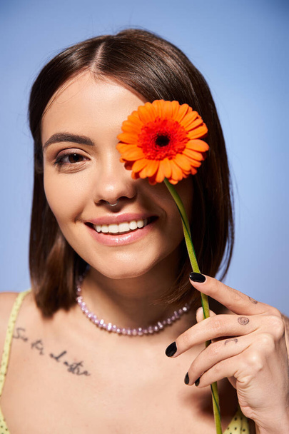 A brunette woman delicately holds a flower in front of her face in a studio setting, connecting with nature. - Foto, immagini