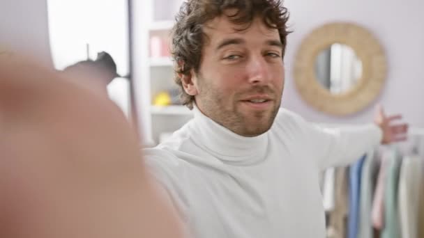 Schöner junger Mann in Rollkragen posiert für ein Selfie in einer hellen Kleiderkammer mit stylischem Kleiderschrank im Hintergrund. - Filmmaterial, Video