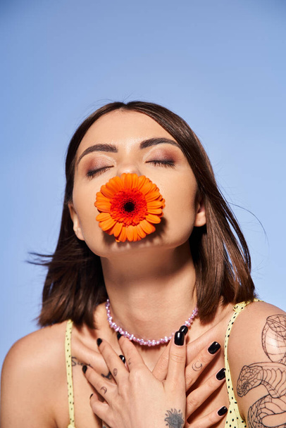 Uma jovem com cabelo morena elegantemente segura uma flor delicada na boca em um estúdio. - Foto, Imagem