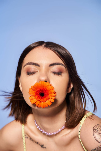 Een jonge vrouw met brunette haar boeiend houdt een bloem in haar mond, presentatie van elegantie en verbinding met de natuur. - Foto, afbeelding