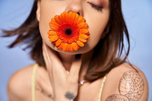 Uma jovem com cabelo morena delicadamente segura uma flor vibrante em sua boca, exalando elegância e graça. - Foto, Imagem