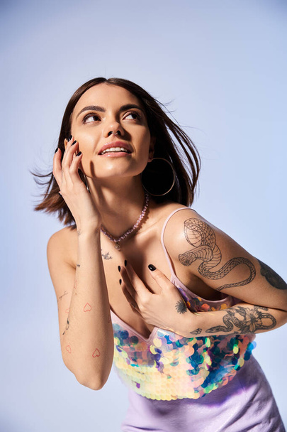 Uma jovem mulher com cabelo morena exibe orgulhosamente suas tatuagens detalhadas em seus braços e peito em um estúdio. - Foto, Imagem