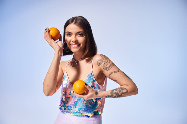 Eine junge Frau mit brünetten Haaren hält in einem Studio zart zwei leuchtende Orangen in den Händen. - Foto, Bild