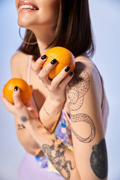 Een jonge vrouw met brunette haar houdt sierlijk twee sinaasappels in haar handen in een studio setting. - Foto, afbeelding