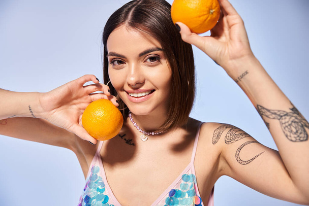 Une femme brune dans un studio tenant deux oranges près de son visage, montrant un lien avec la nature à travers des agrumes vibrants. - Photo, image