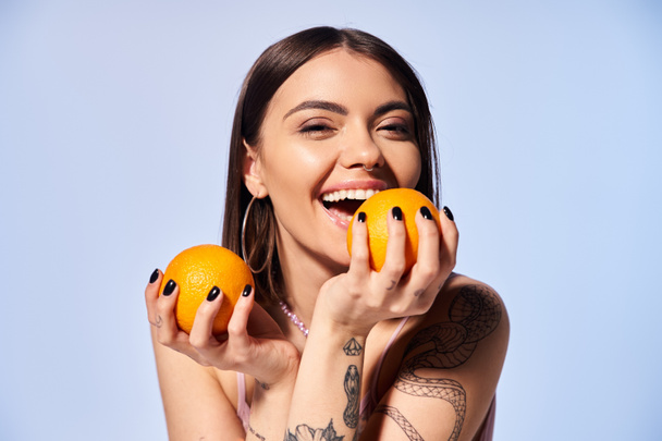 Eine junge Frau mit brünetten Haaren hält zart zwei leuchtende Orangen in ihren Händen. - Foto, Bild