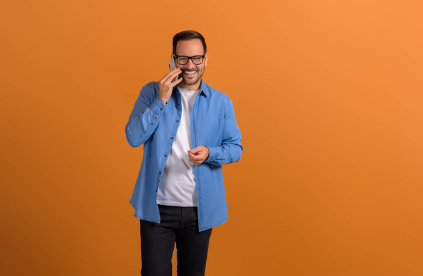 Портрет усміхненого молодого впевненого бізнесмена, який обговорює телефонний дзвінок на помаранчевому фоні - Фото, зображення