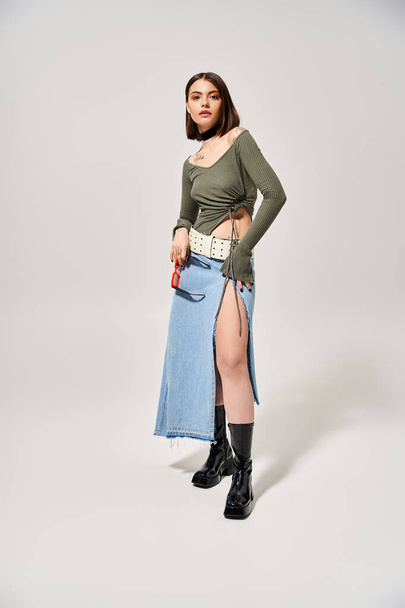 A young woman with brunette hair smiles while posing in a skirt and boots in a studio setting. - Photo, Image