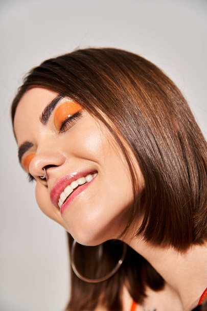 Een jonge vrouw met brunette haar draagt opvallende oranje en zwarte eyeliners op haar gezicht in een studio setting. - Foto, afbeelding