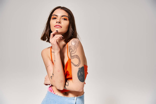 Uma jovem mulher com cabelo morena e tatuagens faz uma pose em um estúdio para uma foto. - Foto, Imagem