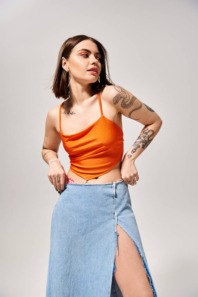 A stylish young woman with brunette hair wearing an orange top and blue skirt in a studio setting. - Photo, Image