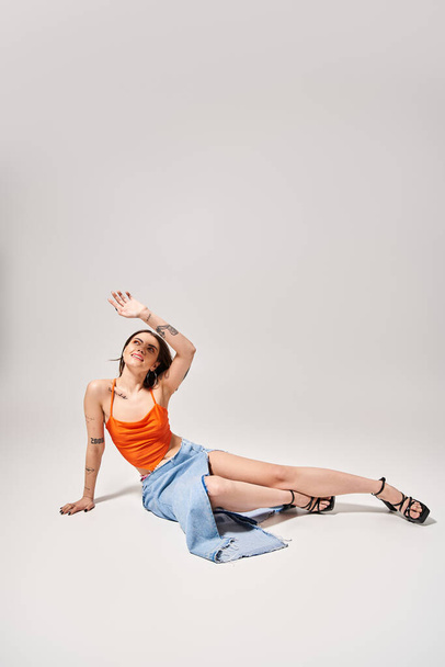 Młoda kobieta z brunetką ubrana w pomarańczowy top spokojnie leży na podłodze w studio. - Zdjęcie, obraz