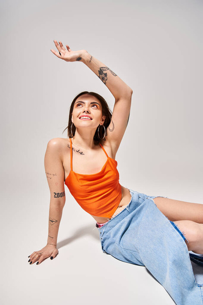 A young woman with brunette hair elegantly dressed in an orange top and blue skirt in a studio setting. - Photo, Image