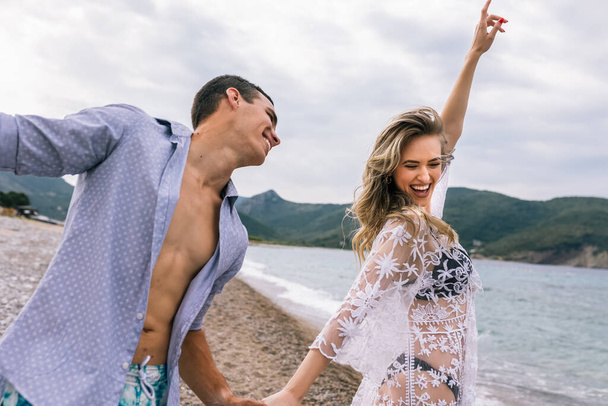 Ευτυχισμένο νεαρό ζευγάρι να γελάει και να αγκαλιάζεται στην παραλία - Φωτογραφία, εικόνα