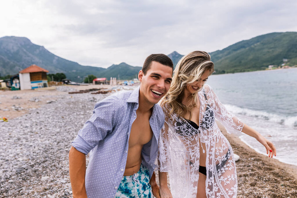 Счастливая молодая пара смеется и обнимается на пляже - Фото, изображение