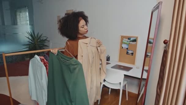 Boční pohled na Latinskou ženu, jak si zkouší kabát a mikinu před zrcadlem, než jde do práce - Záběry, video