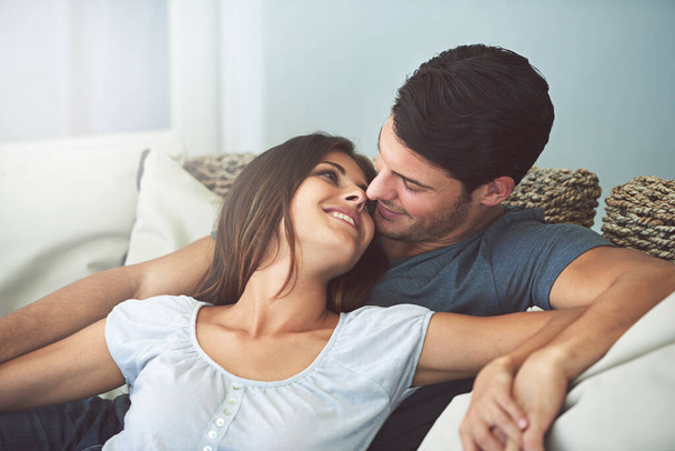 Love, happy and couple relaxing on sofa in living room cuddling and bonding for marriage at home. Smile, romance and young man and woman resting together on couch for care in lounge of modern house - Фото, изображение