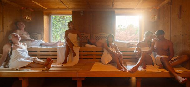 Group of people of various ages relaxing together in hot finnish sauna. dramtic light with Steam, spa and wellness concept. - Photo, Image