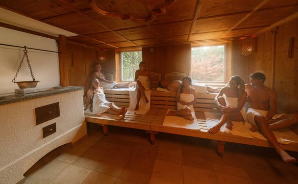ludzie relaksujący się razem relaksują się w gorącej fińskiej saunie. dramatyczne światło z koncepcją Steam, spa i wellness. - Zdjęcie, obraz