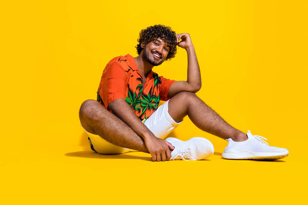 Full length photo of good mood stylish guy wear hawaii shirt white sneakers sitting on floor smile isolated on yellow color background. - Φωτογραφία, εικόνα