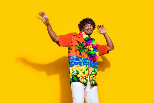 Photo of cheerful carefree man dressed print shirt flower necklace dancing at party hands up isolated on vivid yellow color background. - Foto, afbeelding