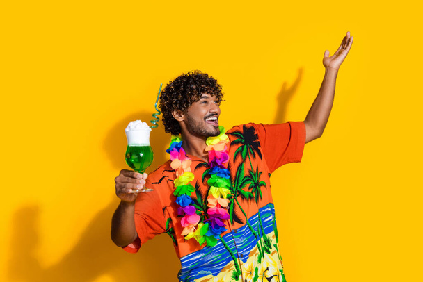 Photo of ecstatic man wear print shirt hold exotic drink raising arm up look empty space isolated on vivid yellow color background. - Valokuva, kuva