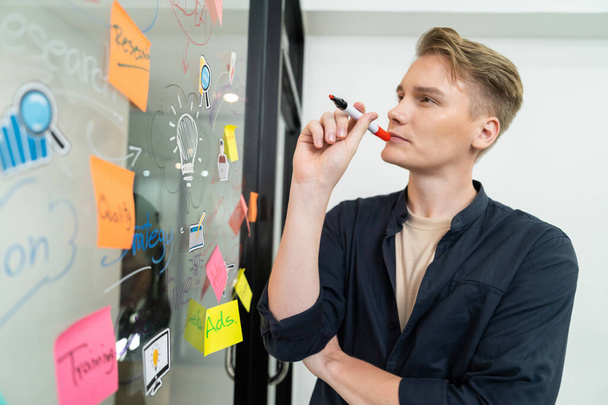 Professional caucasian male leader writing and sharing marketing idea by using mind map and sticky notes on glass board at modern meeting room. Creative business and planing concept. Immaculate. - Photo, Image